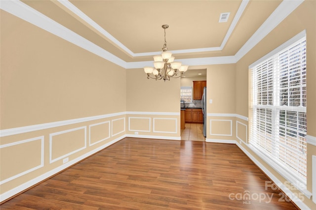 spare room with hardwood / wood-style flooring, ornamental molding, a tray ceiling, and a notable chandelier