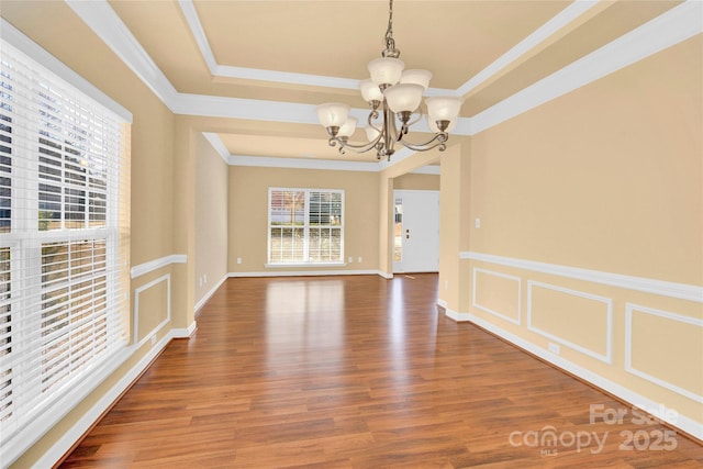 unfurnished dining area featuring ornamental molding, a tray ceiling, wood-type flooring, and a notable chandelier