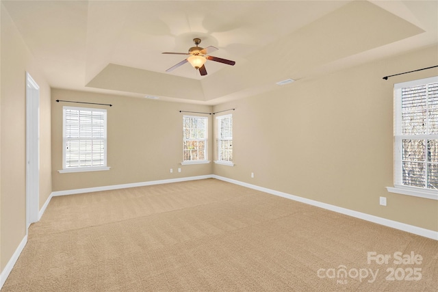 spare room featuring light carpet, a raised ceiling, and ceiling fan