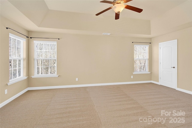 carpeted spare room with a raised ceiling, plenty of natural light, and ceiling fan