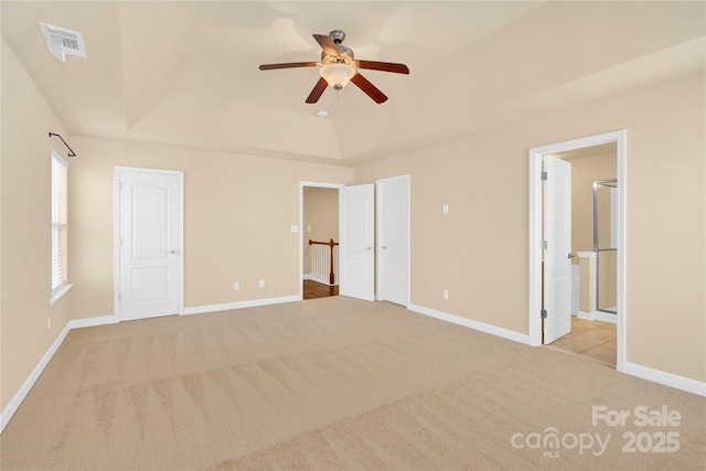 unfurnished bedroom featuring a tray ceiling, ensuite bath, light colored carpet, and ceiling fan