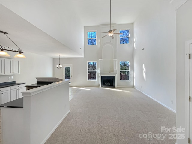 unfurnished living room featuring ceiling fan, light colored carpet, and a towering ceiling