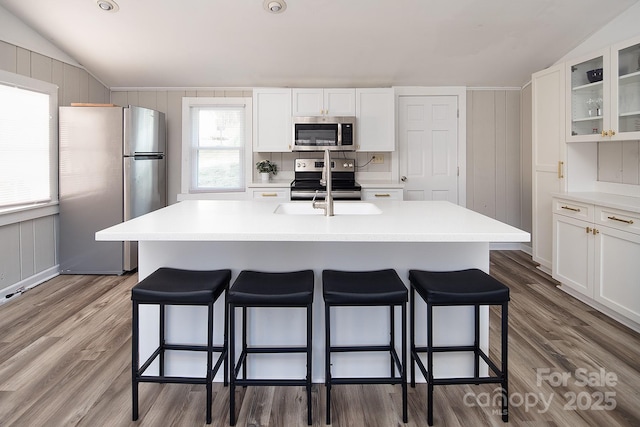 kitchen featuring appliances with stainless steel finishes, a center island with sink, vaulted ceiling, sink, and white cabinetry