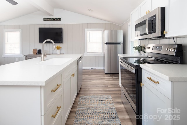 kitchen with sink, appliances with stainless steel finishes, a kitchen island with sink, and lofted ceiling with beams