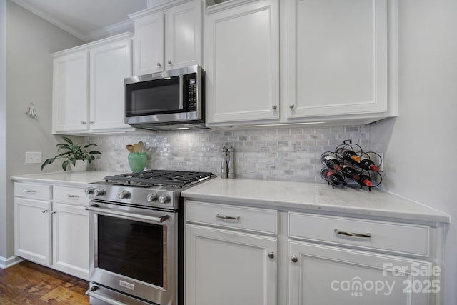 kitchen with crown molding, appliances with stainless steel finishes, white cabinets, light stone countertops, and backsplash