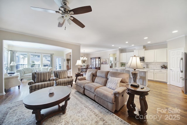 living room featuring ceiling fan with notable chandelier, ornamental molding, and light hardwood / wood-style floors