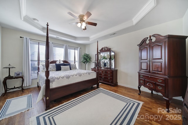 bedroom with a tray ceiling, ornamental molding, dark hardwood / wood-style floors, and ceiling fan