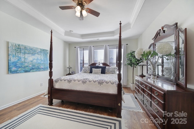 bedroom with crown molding, wood-type flooring, a raised ceiling, and ceiling fan