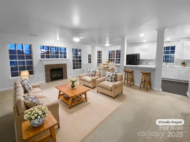 living room with ornate columns, a tiled fireplace, sink, and ceiling fan