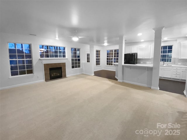 unfurnished living room featuring sink, ornate columns, light colored carpet, ceiling fan, and a fireplace