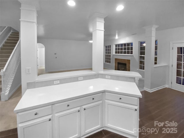 kitchen with a tiled fireplace, ornate columns, kitchen peninsula, and white cabinets