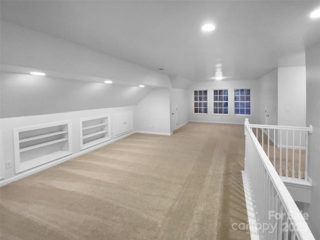 bonus room featuring built in shelves, light colored carpet, and lofted ceiling