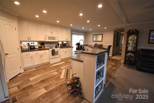 kitchen with white cabinetry, an island with sink, sink, light hardwood / wood-style floors, and white appliances