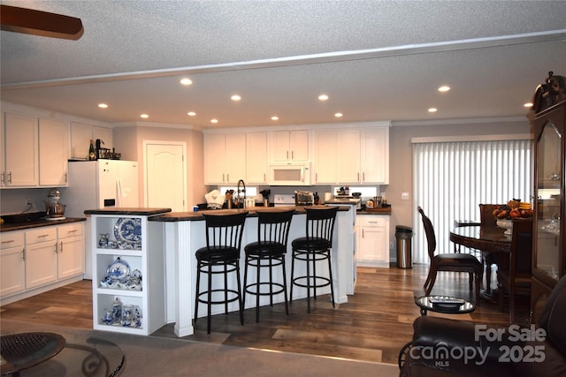 kitchen with white cabinets, a kitchen breakfast bar, dark hardwood / wood-style flooring, a kitchen island with sink, and white appliances