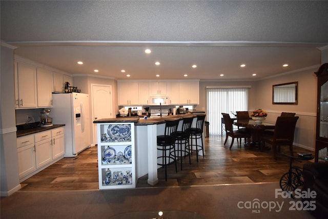 kitchen with white appliances, a kitchen breakfast bar, a center island with sink, and white cabinets