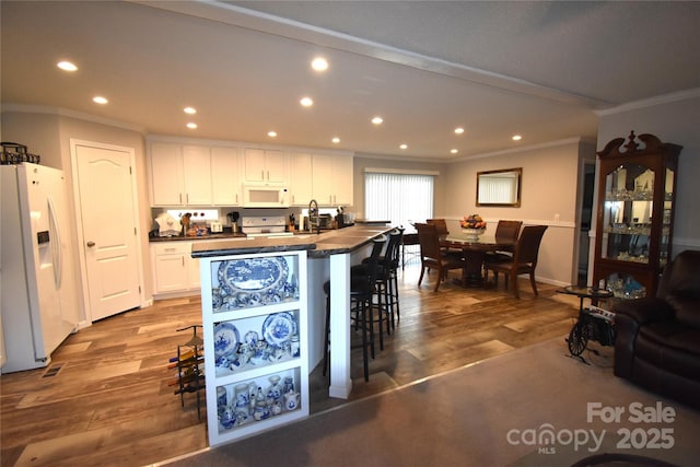 kitchen featuring wood finished floors, dark countertops, white appliances, and white cabinets