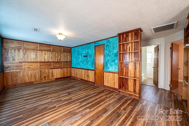 unfurnished living room featuring dark wood-type flooring, a textured ceiling, and wood walls