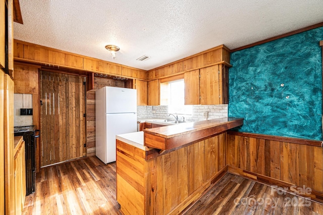 kitchen with dark hardwood / wood-style flooring, wooden walls, kitchen peninsula, and white fridge