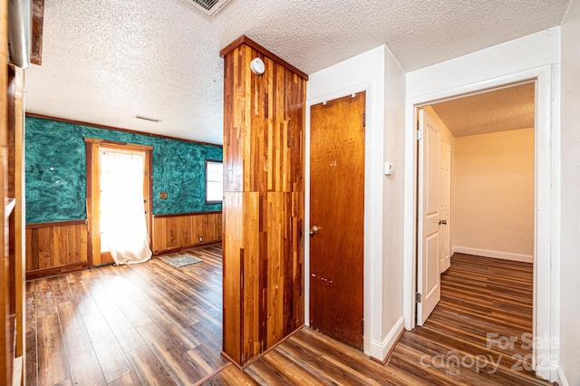 corridor featuring dark wood-type flooring, wooden walls, and a textured ceiling