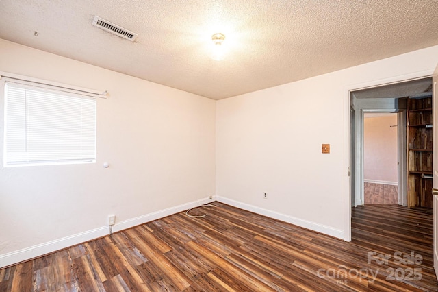 spare room featuring a textured ceiling and dark hardwood / wood-style flooring