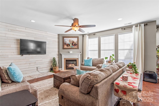 living room with light hardwood / wood-style floors, ceiling fan, and wood walls