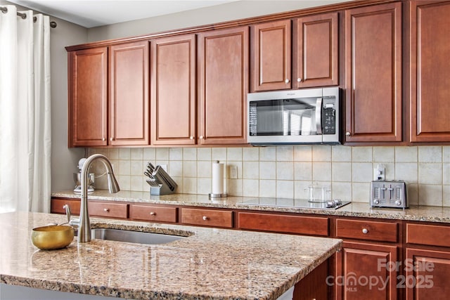 kitchen featuring light stone countertops, sink, black electric stovetop, and backsplash