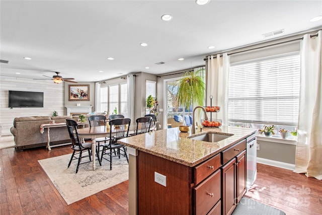 kitchen with sink, dishwasher, light stone countertops, a center island with sink, and dark hardwood / wood-style flooring