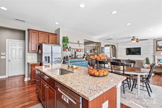 kitchen featuring sink, appliances with stainless steel finishes, dark hardwood / wood-style floors, light stone countertops, and a kitchen island with sink