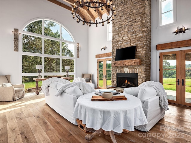 living room with hardwood / wood-style floors, a stone fireplace, high vaulted ceiling, and french doors