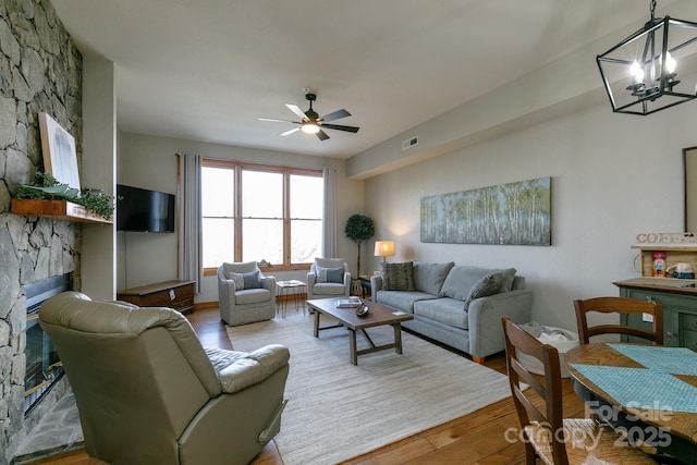 living room featuring ceiling fan with notable chandelier, a fireplace, and light hardwood / wood-style floors