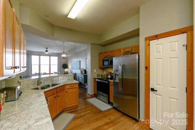 kitchen featuring appliances with stainless steel finishes, pendant lighting, sink, light stone counters, and light wood-type flooring