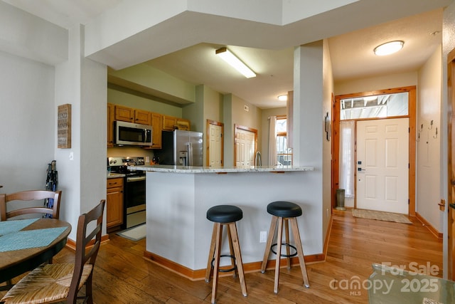 kitchen with light stone counters, stainless steel appliances, a kitchen bar, and light hardwood / wood-style floors