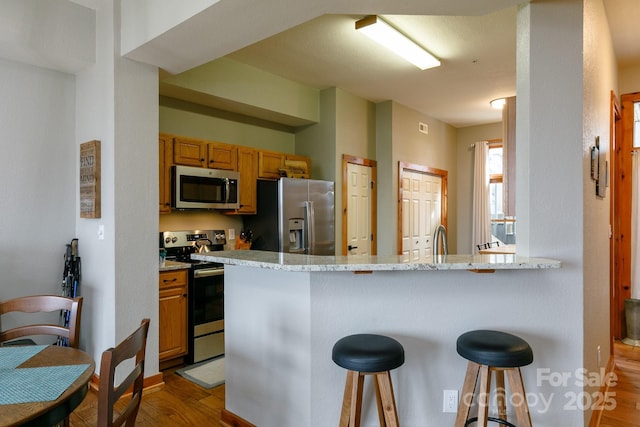 kitchen with appliances with stainless steel finishes, a kitchen breakfast bar, light stone countertops, kitchen peninsula, and light wood-type flooring