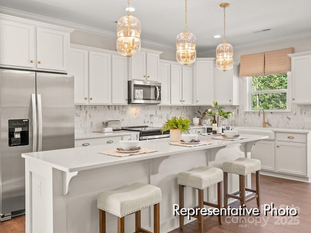 kitchen featuring hanging light fixtures, stainless steel appliances, white cabinets, and a kitchen island