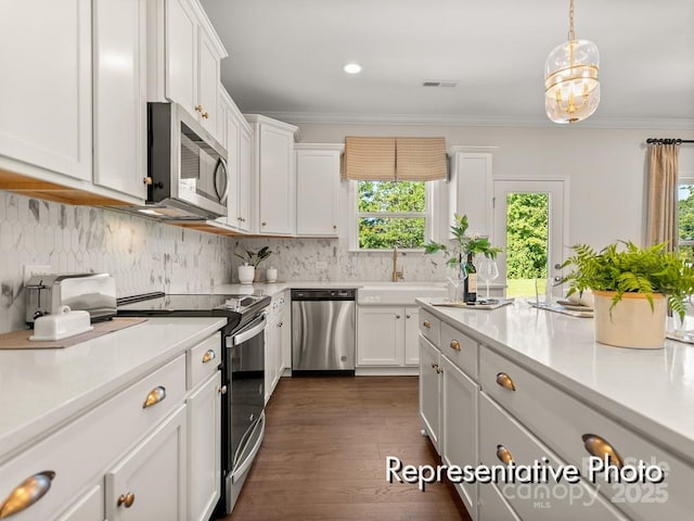 kitchen featuring appliances with stainless steel finishes, decorative light fixtures, tasteful backsplash, white cabinets, and crown molding