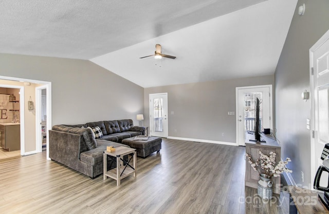 living room with ceiling fan, lofted ceiling, light hardwood / wood-style flooring, and a textured ceiling