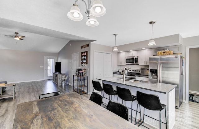 kitchen with sink, decorative light fixtures, appliances with stainless steel finishes, a kitchen breakfast bar, and light stone countertops