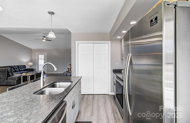 kitchen with appliances with stainless steel finishes, white cabinetry, sink, hanging light fixtures, and light hardwood / wood-style flooring