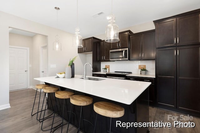 kitchen featuring sink, appliances with stainless steel finishes, a kitchen island with sink, hanging light fixtures, and a kitchen bar