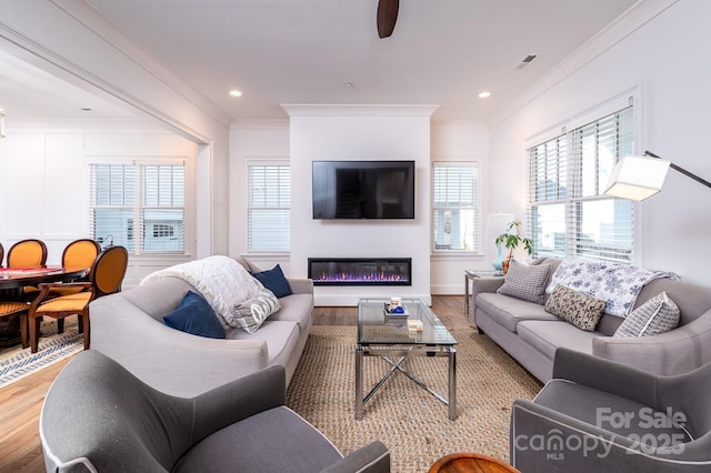 living area featuring light wood finished floors, recessed lighting, visible vents, ornamental molding, and a glass covered fireplace