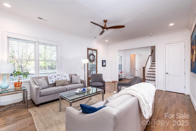 living room featuring light wood-style floors, stairs, visible vents, and crown molding