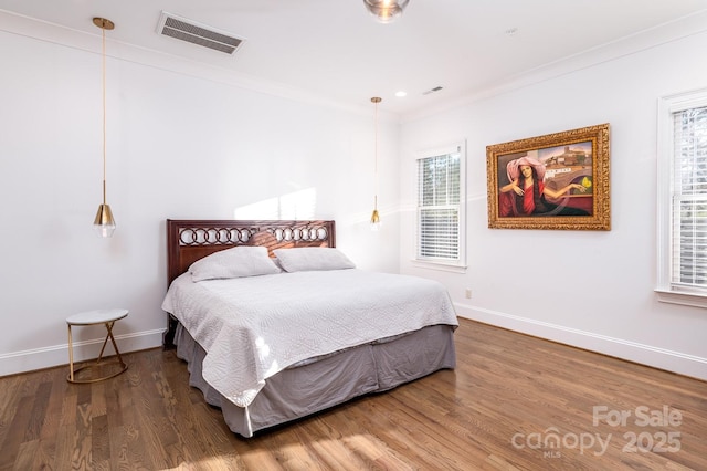 bedroom with baseboards, crown molding, visible vents, and wood finished floors