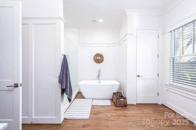 bathroom featuring visible vents, wood finished floors, crown molding, a freestanding bath, and a decorative wall