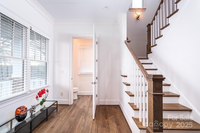 staircase with ornamental molding, wood finished floors, and baseboards