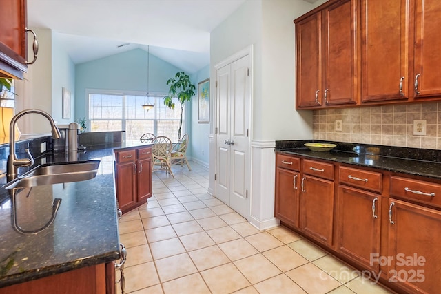 kitchen with vaulted ceiling, tasteful backsplash, sink, dark stone countertops, and hanging light fixtures