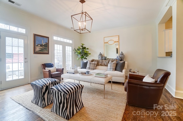 living room featuring a notable chandelier, hardwood / wood-style flooring, ornamental molding, and a healthy amount of sunlight