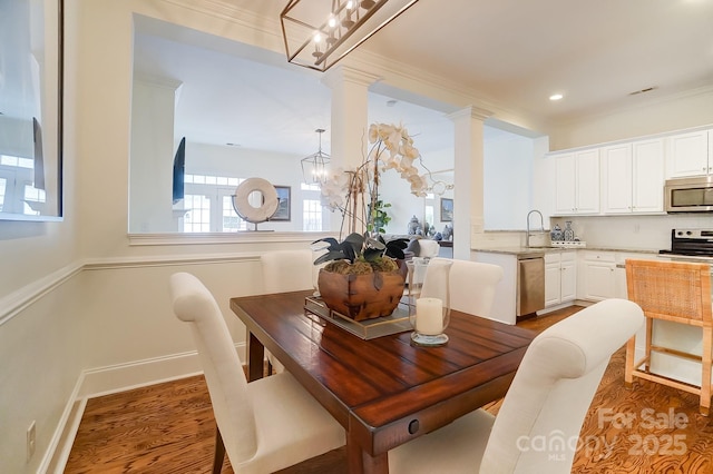 dining space with sink, ornate columns, ornamental molding, a notable chandelier, and hardwood / wood-style flooring