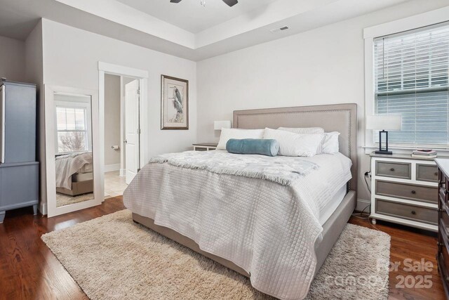 bedroom featuring a raised ceiling, dark hardwood / wood-style floors, and ceiling fan