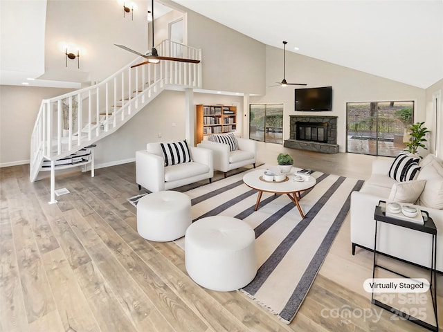 living room with hardwood / wood-style flooring, a stone fireplace, high vaulted ceiling, and ceiling fan