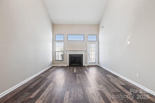 unfurnished living room featuring dark wood-type flooring and a towering ceiling